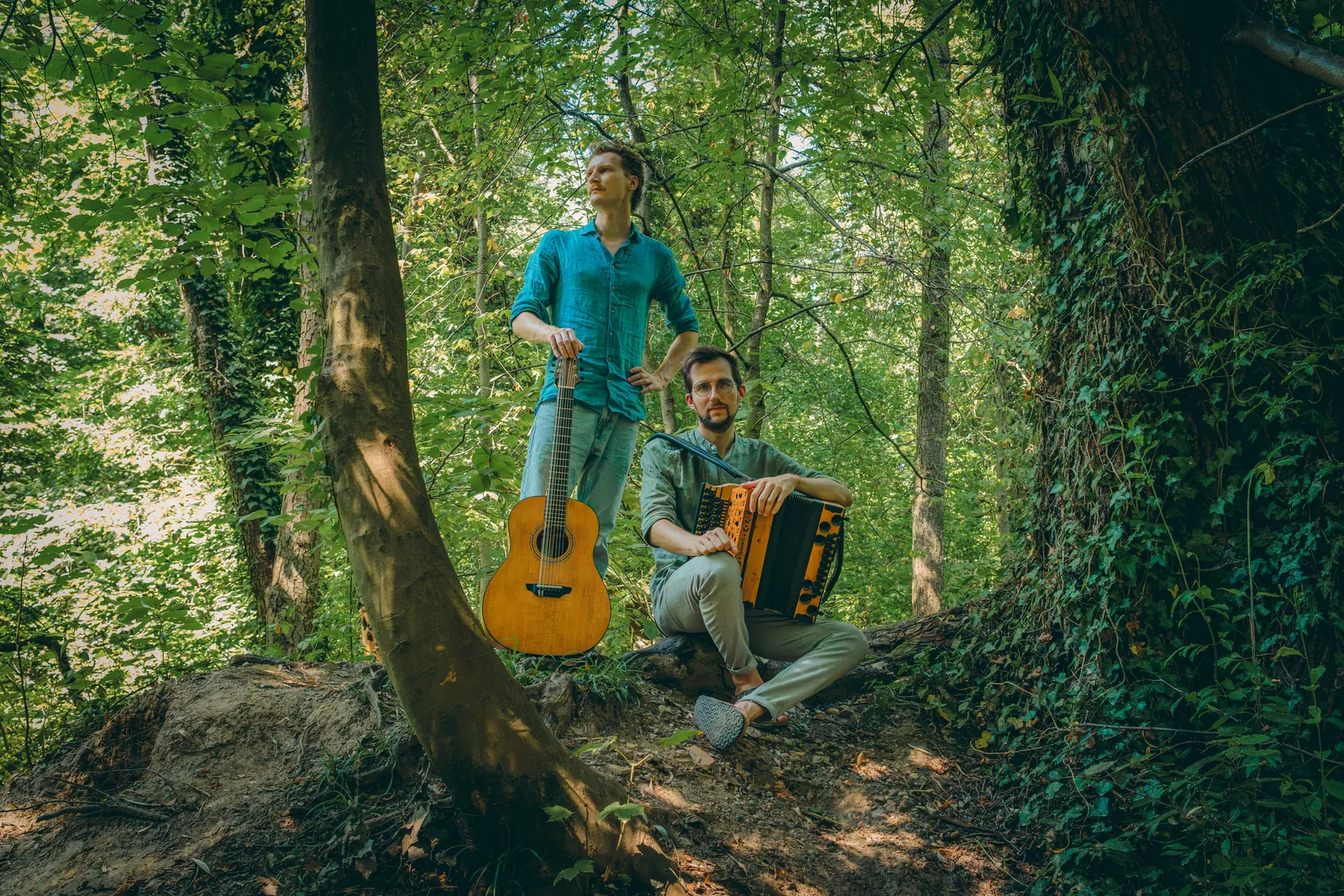 Timmy with his guitar and Jonny with his Styrian accordion in a sunlit forest