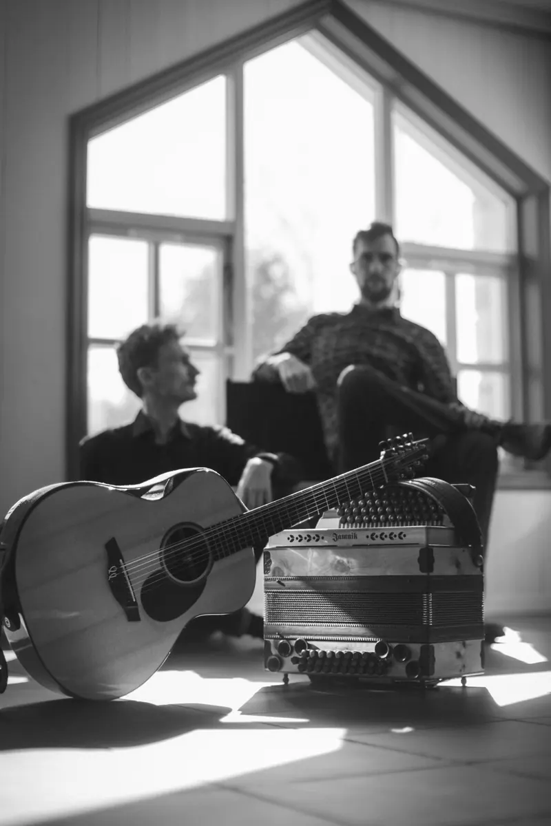 Schwarzweißporträt des Duos am Fenster mit den Instrumenten